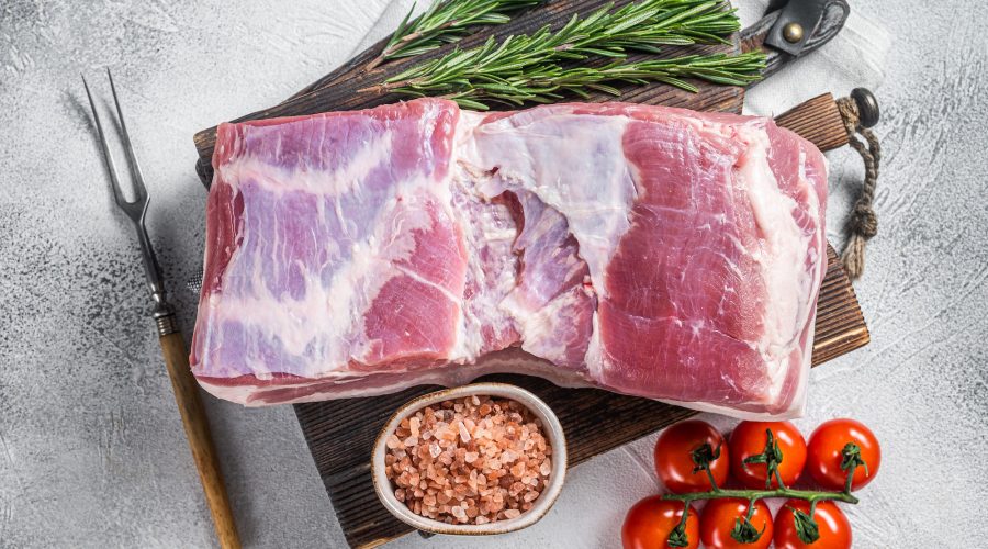 Pork belly block, raw meat with skin on a wooden board with rosemary. White background. Top view