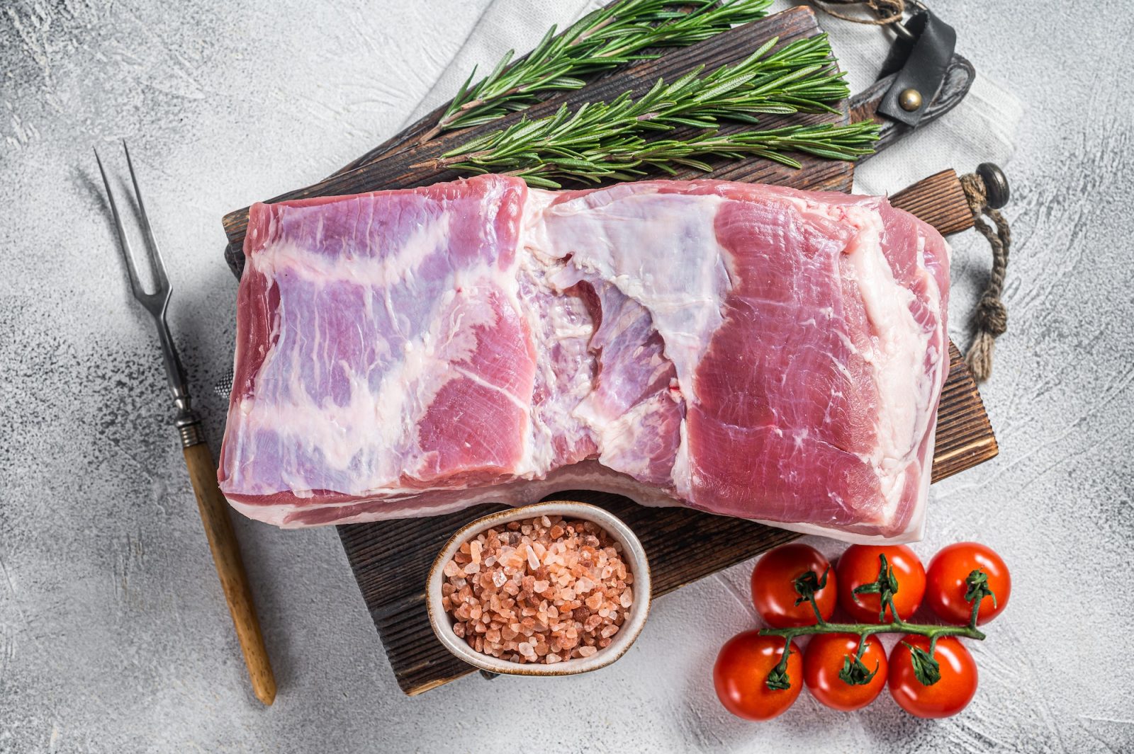 Pork belly block, raw meat with skin on a wooden board with rosemary. White background. Top view